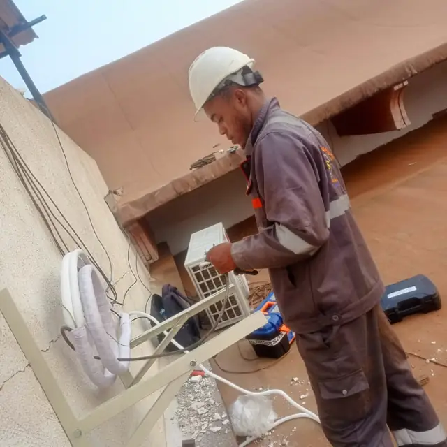 Technicien SOS Frigoriste en tenue et casque, raccordant une clim sur une terrasse